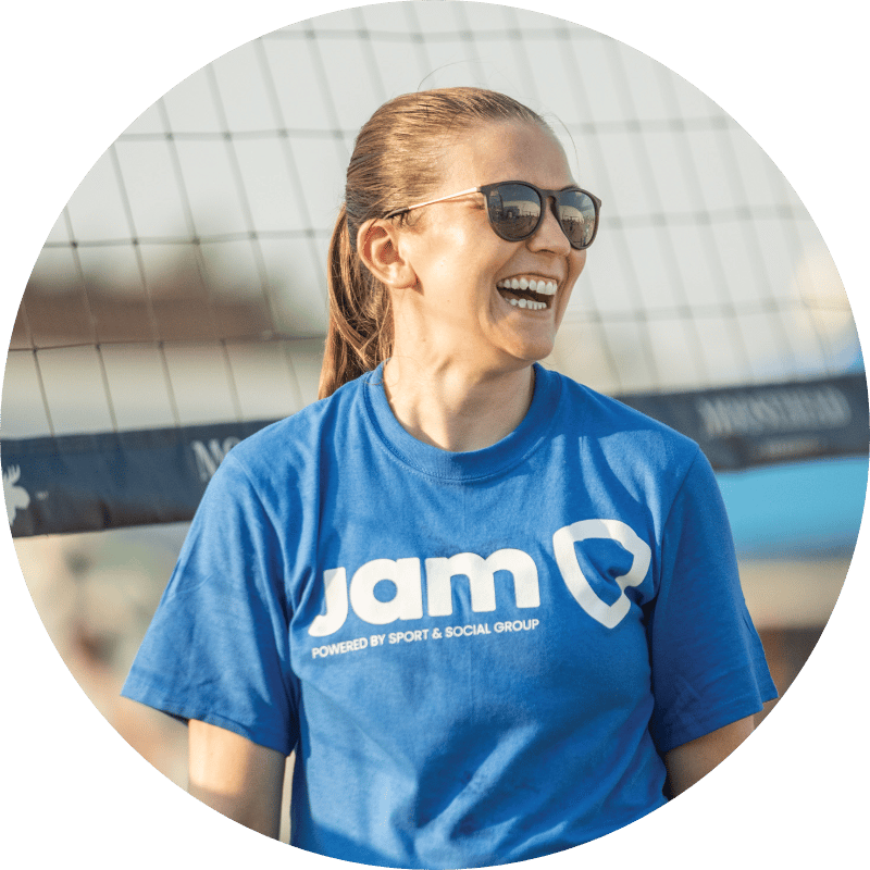 Woman laughing on a beach volleyball court wearing a royal blue JAM t-shirt