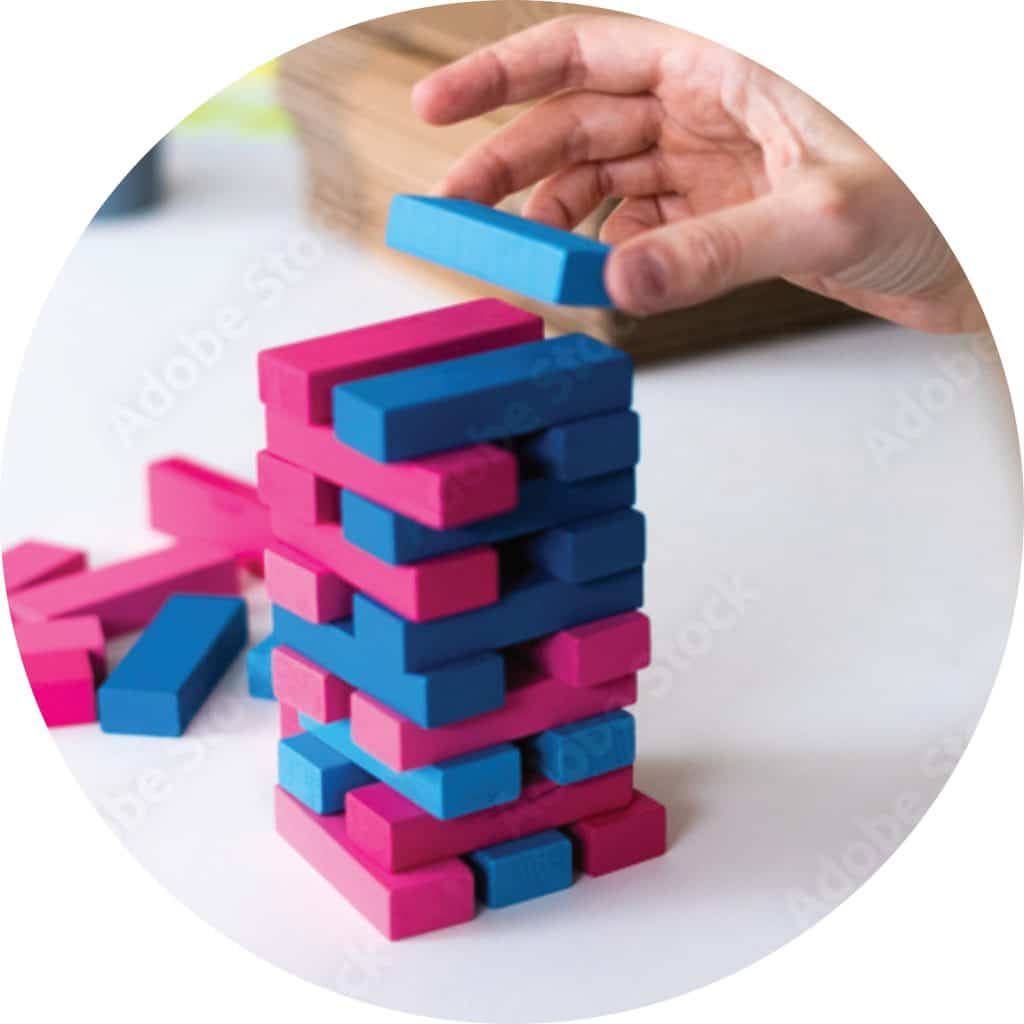Play at work enables creative thinking, builds trust and ignites free-flowing energy. Person building a hot pink and sky blue Jenga tower. 