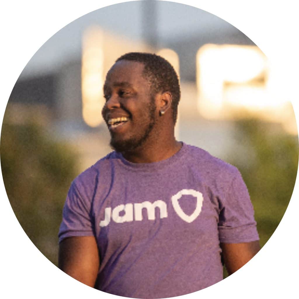 Workplace play promotes physical and mental health, reduces stress and burnout. African-Canadian Man in purple JAM t-shirt walking outside and smiling.